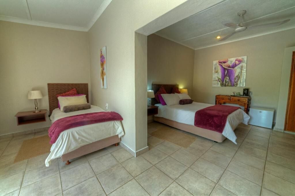 Une chambre d’hôtel avec deux lits, une table de chevet, une lampe, un radiateur et des œuvres d’art accrochées aux murs.