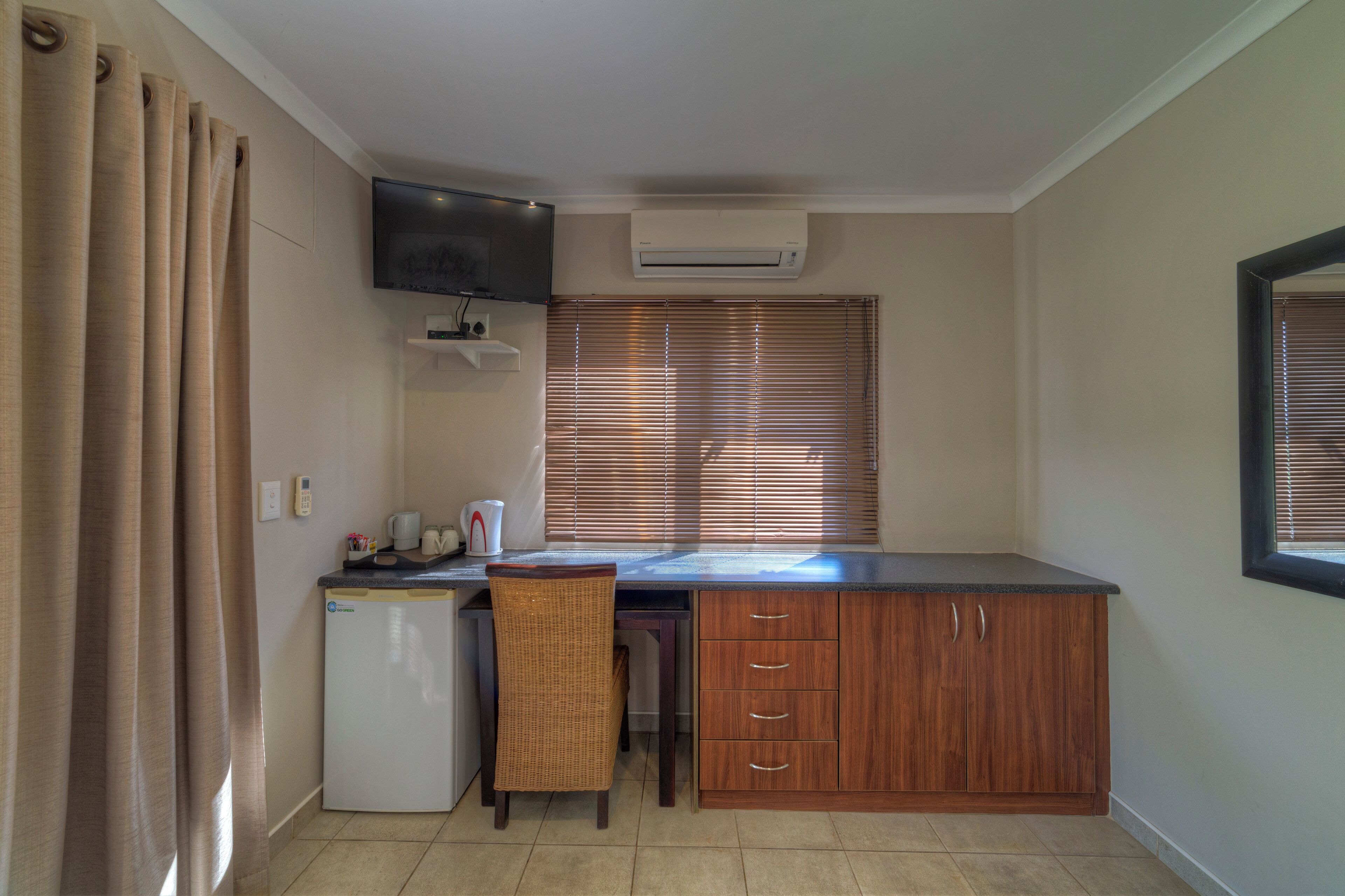 Cozinha compacta com geladeira, cafeteira e televisão fixada na parede.