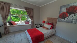 A bedroom with a bed, a window seat, a bedside table, a lamp, and a painting.