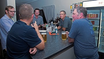 A group of people at a bar with a refrigerator stocked with beverages.