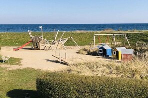 A beach playground with a slide and swings, a small shed, and a clear view of the ocean. - Holiday home in Süssau with swimming pool (Süssau)