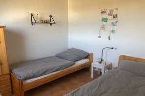 A single-bed room with a wooden bed, a small bedside table with a lamp, and a wall-mounted shelf with decorative items. - Holiday home in Süssau with swimming pool (Süssau)
