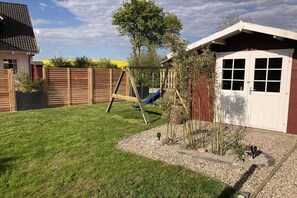 A backyard with a swing set, a small garden with plants, and a shed. - Holiday home in Süssau with swimming pool (Süssau)