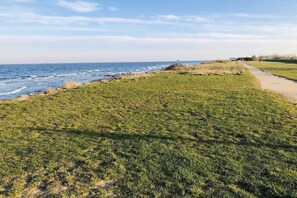 A grassy area with a path leading to the sea, a clear sky, and a distant view of the ocean. - Holiday home in Süssau with swimming pool (Süssau)