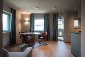 A modern interior with a round dining table, two chairs, a sofa, and a kitchen area. - New, cozy apartment in a central location featuring Italian design and mountain views (Mühlbach)