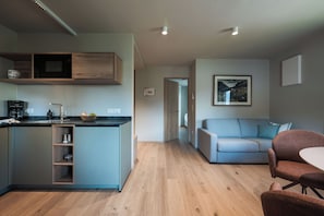 A modern kitchen with a built-in island, a dining area with a table and chairs, and a living room with a sofa. - New, cozy apartment in a central location featuring Italian design and mountain views (Mühlbach)