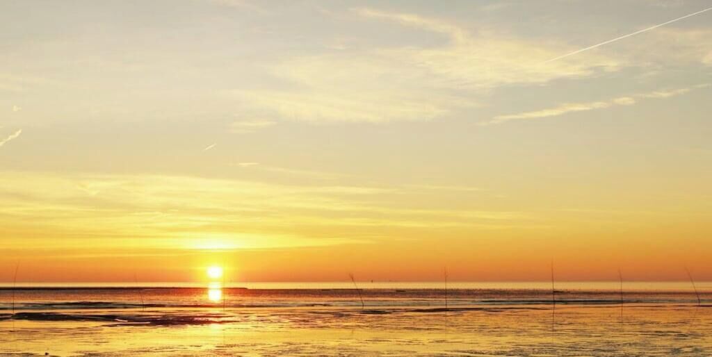 Un atardecer sobre una playa con aguas tranquilas y un cielo despejado.