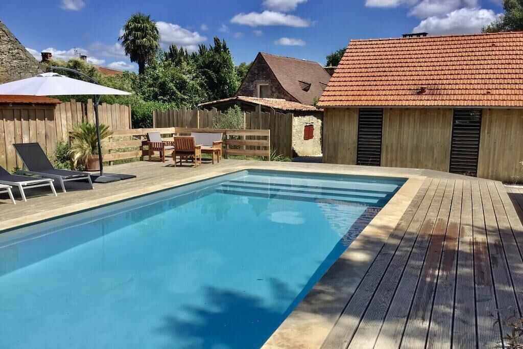 Piscina com deck de madeira, espreguiçadeiras e uma pequena mesa.
