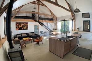 A spacious loft with a central kitchen island, a staircase leading to an upper level, and a large window providing natural light. - The chair and the pool near Sarlat (Veyrines-de-Domme)