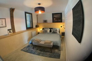 Un dormitorio con una cama, lámparas de noche, un banco, una ventana con persianas y una obra de arte en la pared.