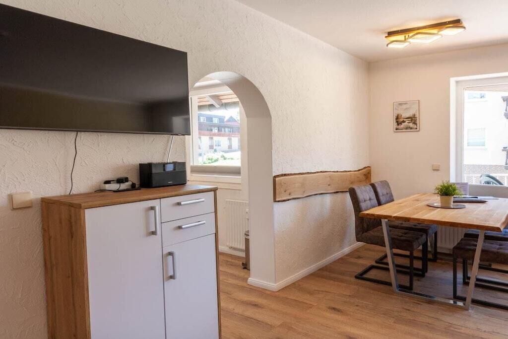 A compact kitchen with a built-in fridge, a wooden dining table with benches, and a large window providing natural light.
