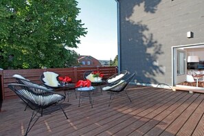 Een terras buiten, met houten vloer, metalen stoelen, een kleine tafel met een bloevas en een glas rode wijn.