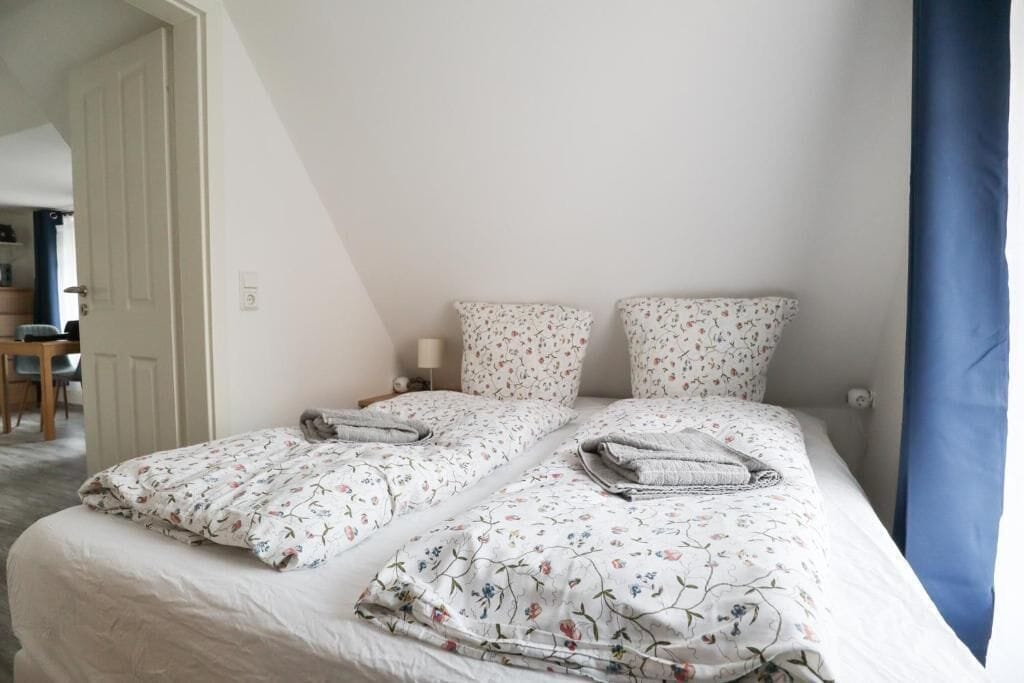 Ein Schlafzimmer mit zwei Betten, jeweils mit Blumenbettwäsche und Kissen, einem Nachttisch mit Lampe und einer Tür zu einem weiteren Raum.