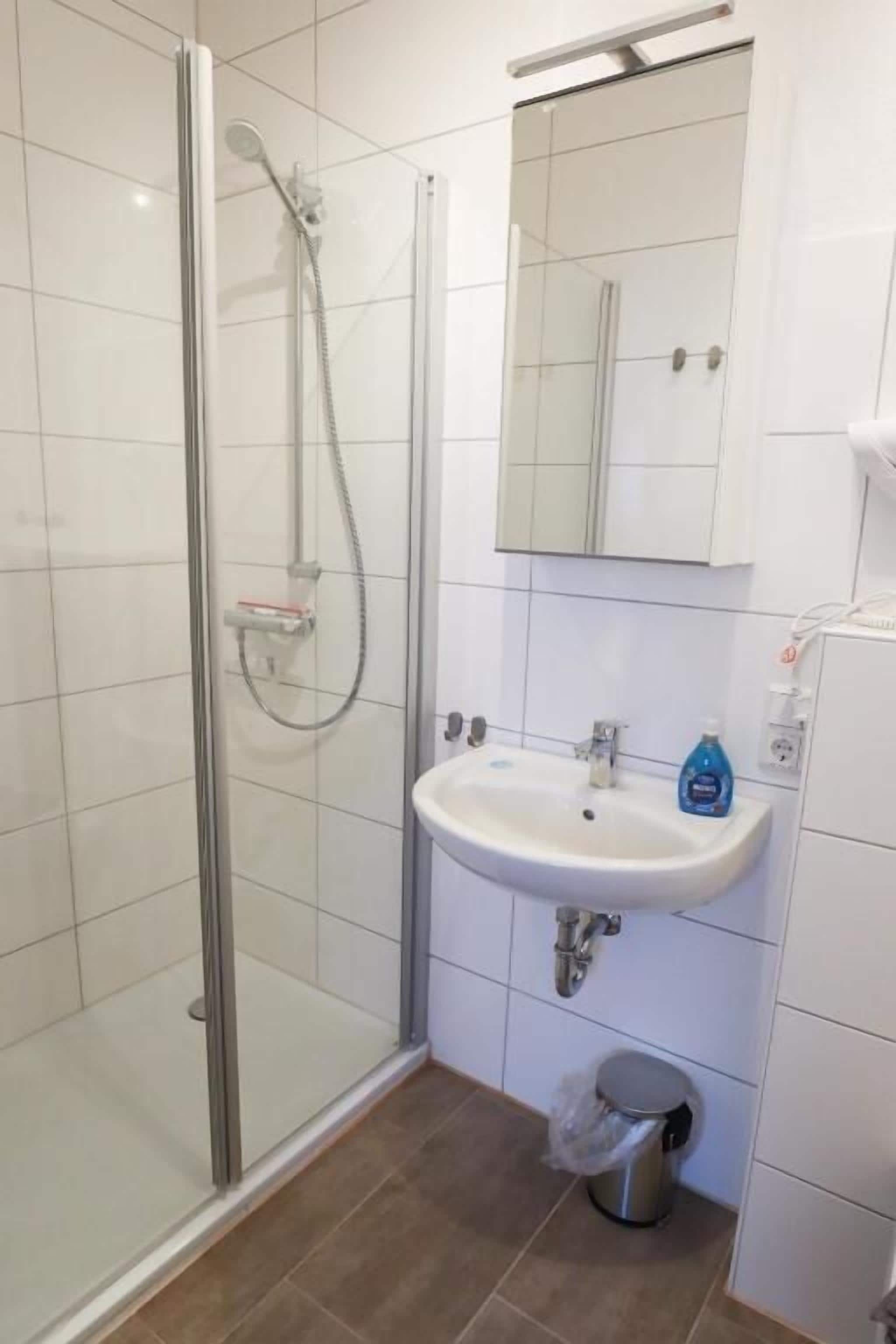 Ein Badezimmer mit Duschkabine aus Glas, Waschbecken und Spiegel.