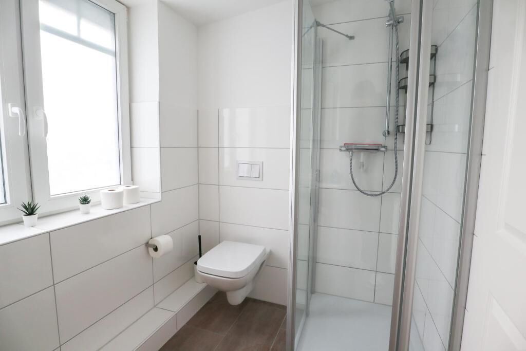Ein Badezimmer mit Toilette, Duschkabine und einem Fenster mit Pflanze.