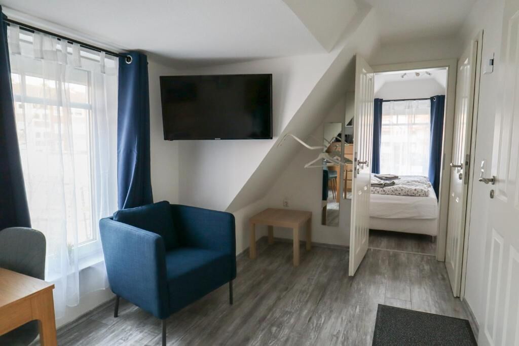 Ein kleines Zimmer mit einem Bett, einem Sessel, einem kleinen Tisch, einem an der Wand montierten Fernseher und einer Treppe, die zu einem weiteren Raum führt.
