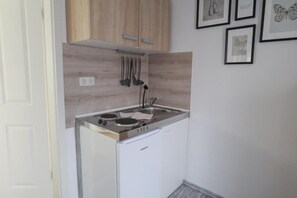 A compact kitchen with a built-in stove, white cabinets, and a wall-mounted utensil rack.