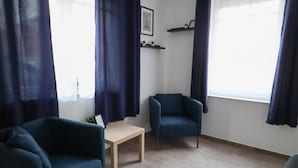 Quarto com sofá, cadeira, mesa pequena e janela com cortinas.