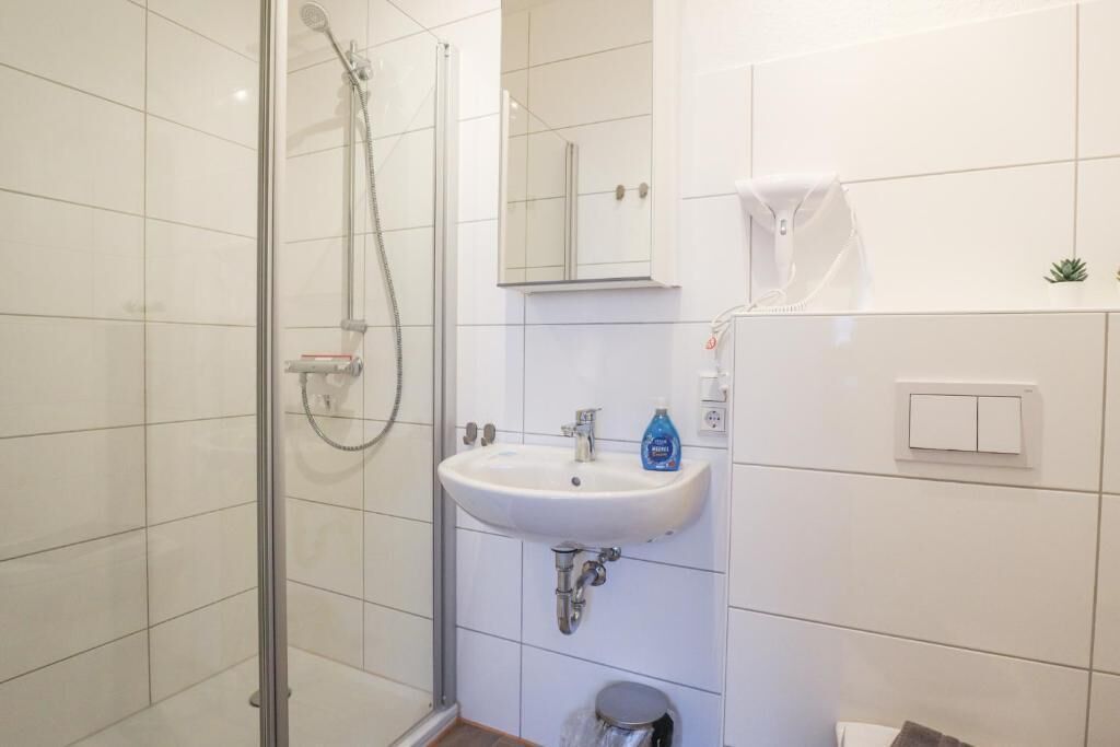 Un baño con ducha de vidrio, lavamanos blanco y espejo arriba.
