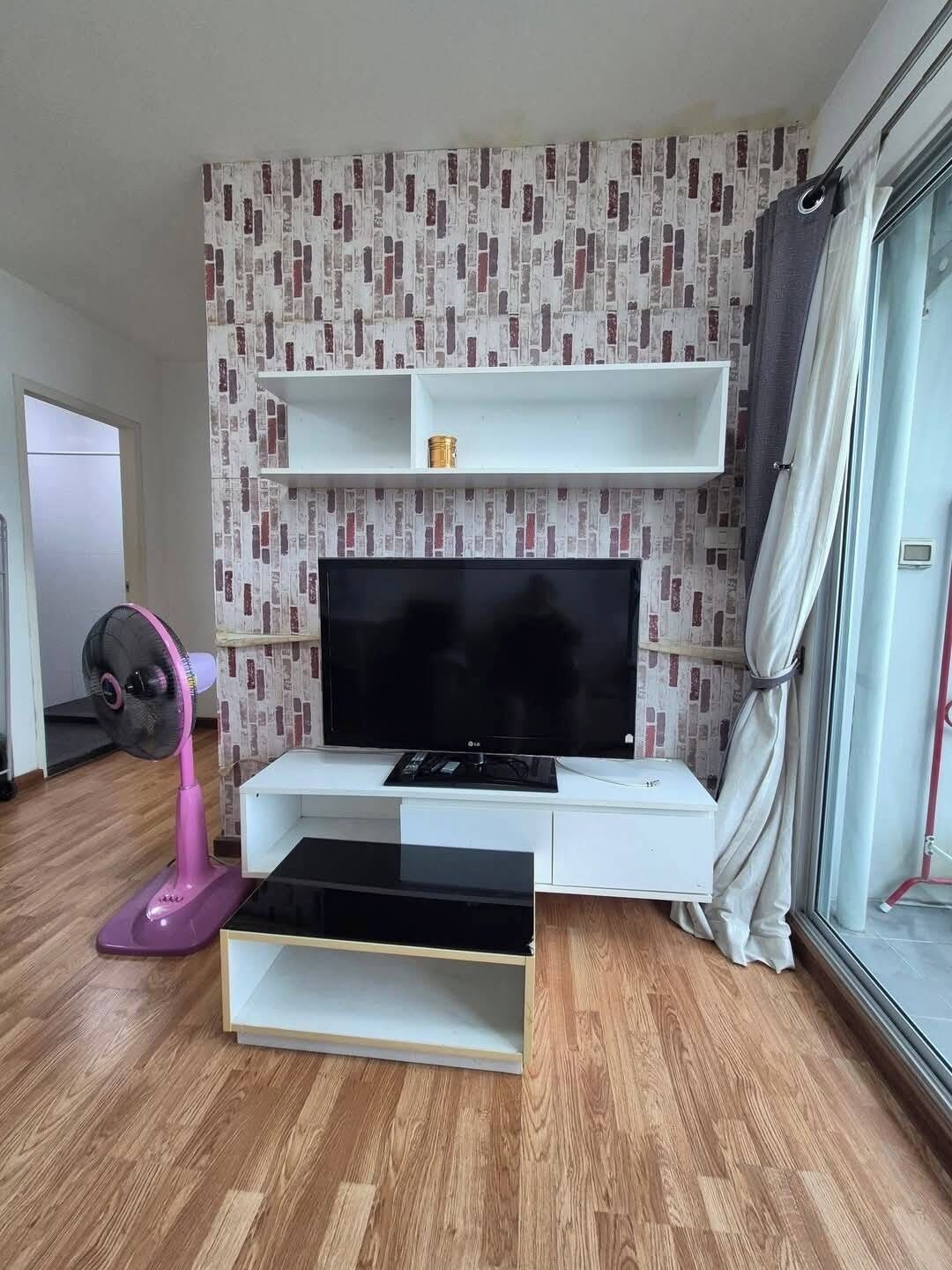 Un salón moderno con un televisor de pantalla plana, mueble de entretenimiento blanco y un ventilador rosa.