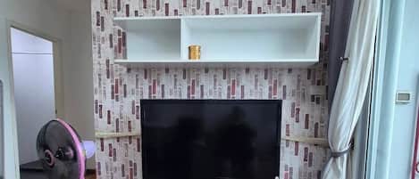 A modern living room with a flat-screen TV, white entertainment unit, and a pink fan.