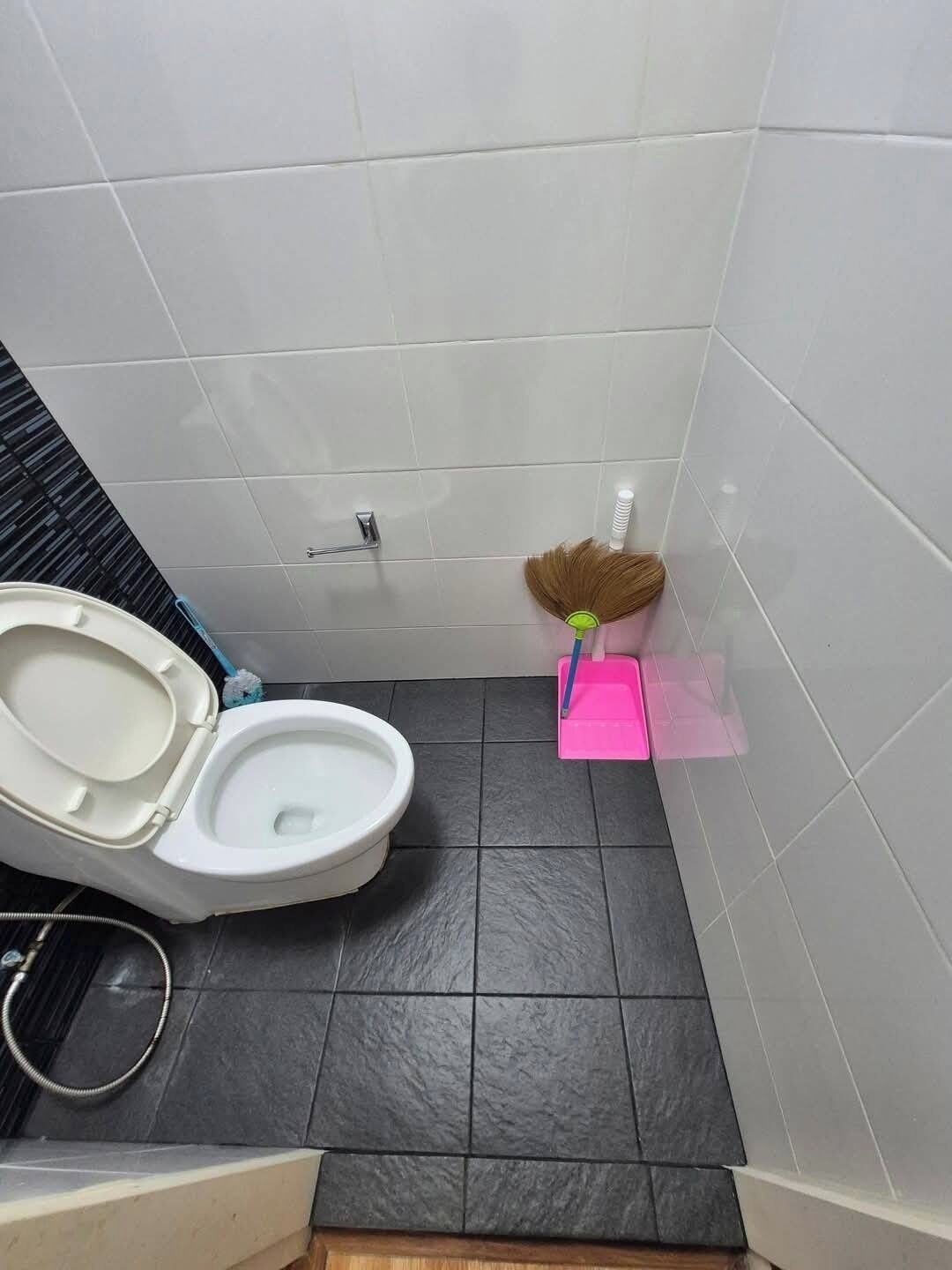 Ein Badezimmer mit Toilette, einem Besen und einem rosa Halter für Putzbürsten.