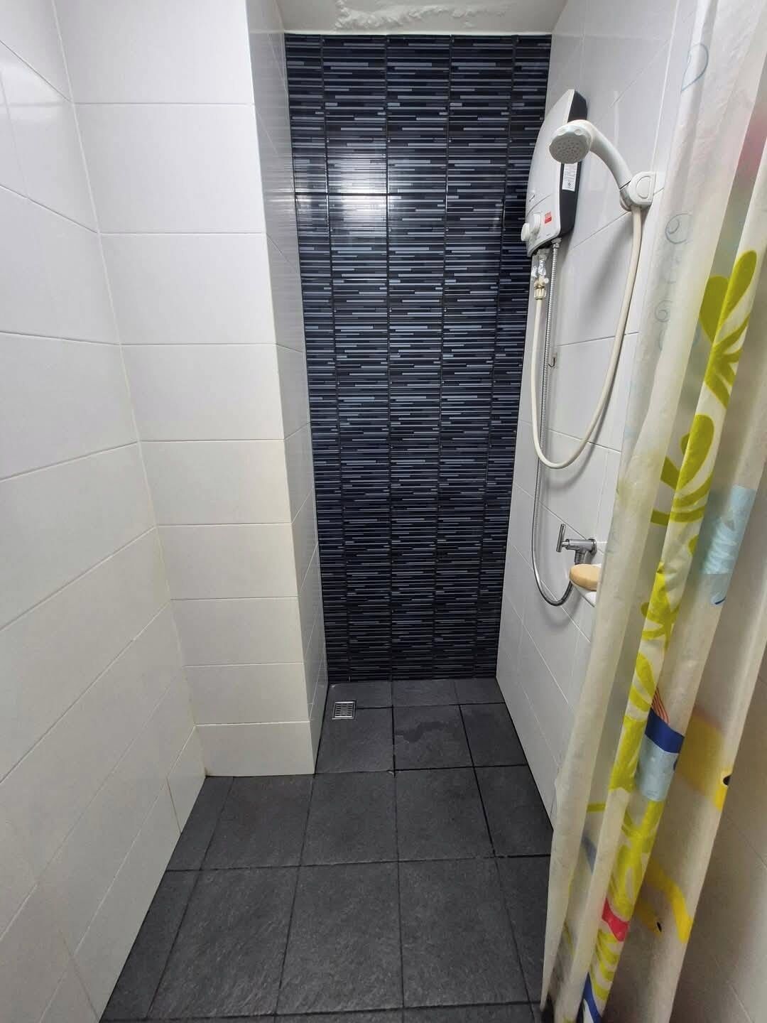 A small bathroom with white tiled walls, a black tiled shower enclosure, and a showerhead.