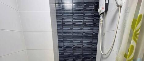 A small bathroom with white tiled walls, a black tiled shower enclosure, and a showerhead.