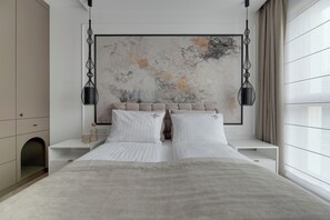 Un dormitorio moderno con una cama grande, ropa de cama blanca, un cuadro de pared con textura y un diseño minimalista.
