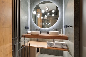 A modern bathroom with two sinks, a large mirror, and a wooden shelf with towels. - Porto Seaside with Gym and Parking (Gdańsk)