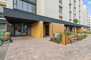 A modern building with a flat roof, large windows, and a paved entrance area with a bench and planter. - Porto Seaside with Gym and Parking (Gdańsk)