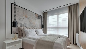 Quarto moderno com uma cama grande, mesa de cabeceira, pintura abstrata na parede e janela com cortinas.