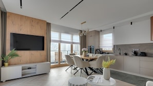 Cozinha moderna com área de refeições, televisão de tela plana fixada numa parede de madeira e uma janela grande que proporciona iluminação natural.