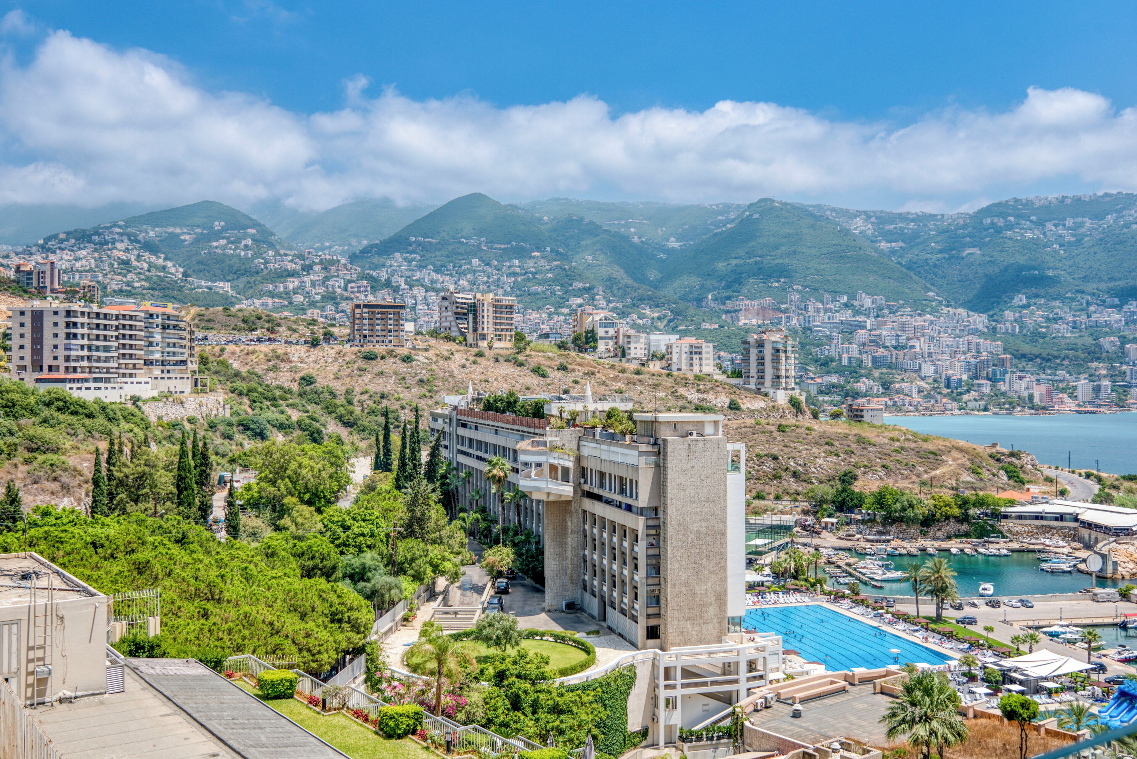 A coastal cityscape with a prominent hotel featuring a rooftop pool and a view of the sea.