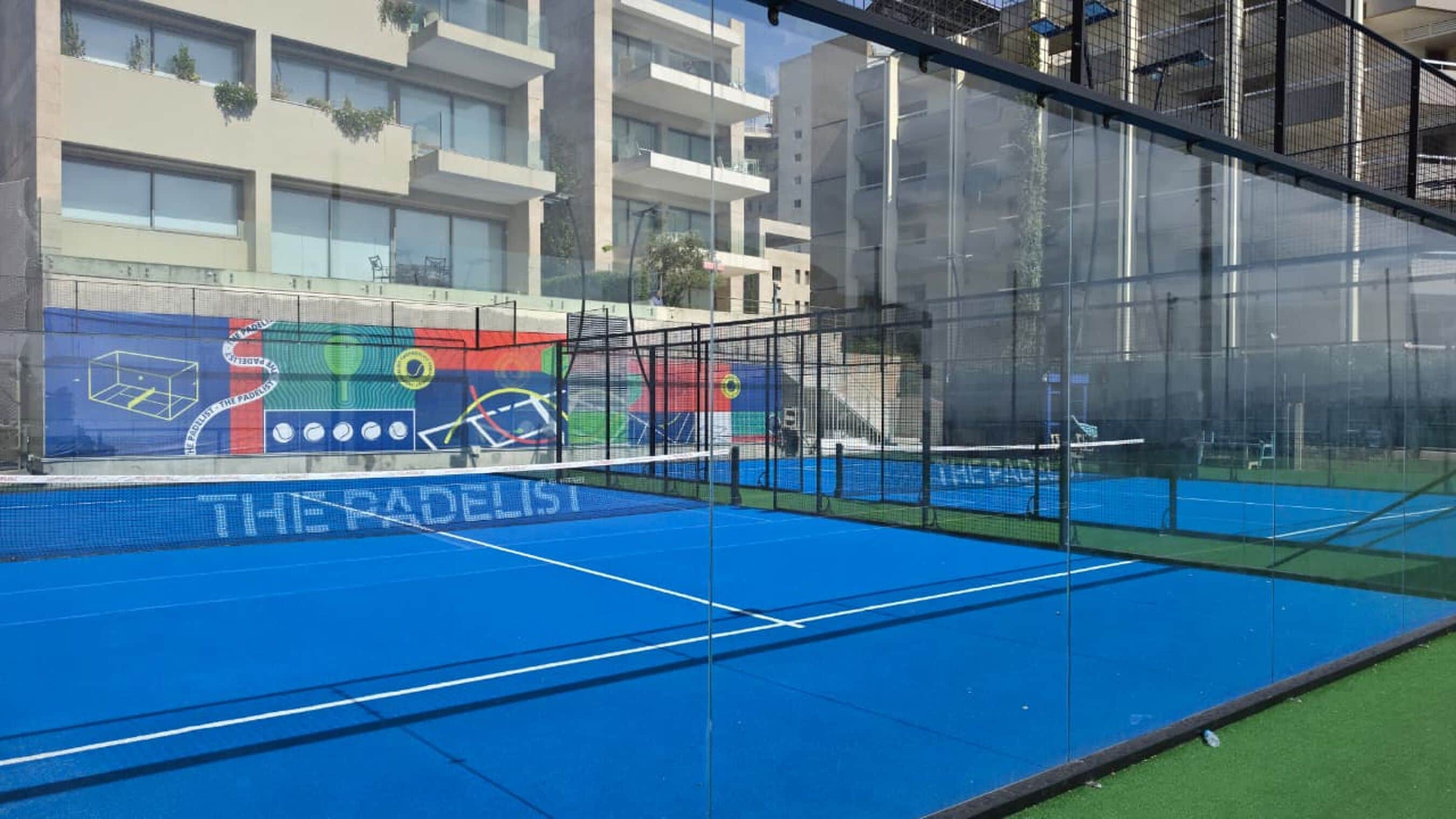 A tennis court with a net, surrounded by a fence, and a mural on the wall.