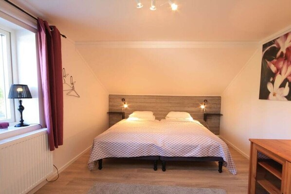 A bedroom with a bed, a window with curtains, a lamp, a wall-mounted light, and a painting. - Holiday home in Sandhem with swimming pool (Sandhem)