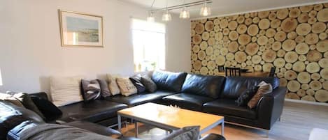 A living room with a black leather sofa, a wooden coffee table, and a wall decorated with wooden logs.