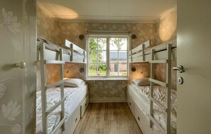 Ein kleines Zimmer mit zwei Etagenbetten, einem Fenster mit Blick auf Grünflächen und einer Tür mit einem runden Griff.