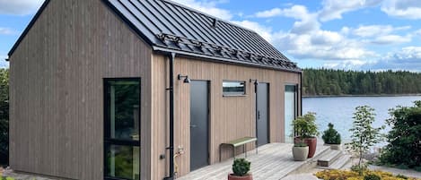 A modern wooden cabin with a sloped roof, large windows, and a deck with potted plants.