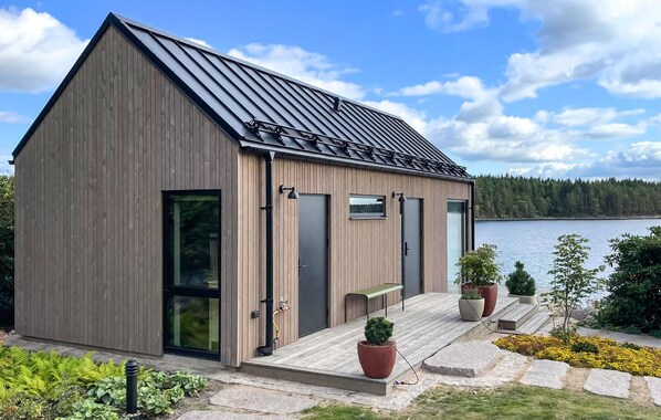 Eine moderne Holzjagdhaushütte mit geneigtem Dach, großen Fenstern und einer Terrasse mit Topfpflanzen.