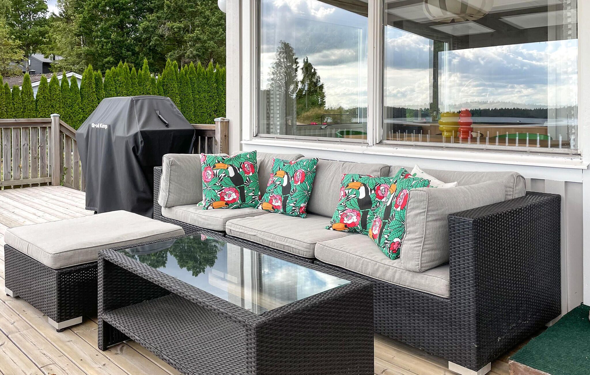 Un espace extérieur abrité avec des sièges, une table à plateau en verre, des canapés confortables et un barbecue.