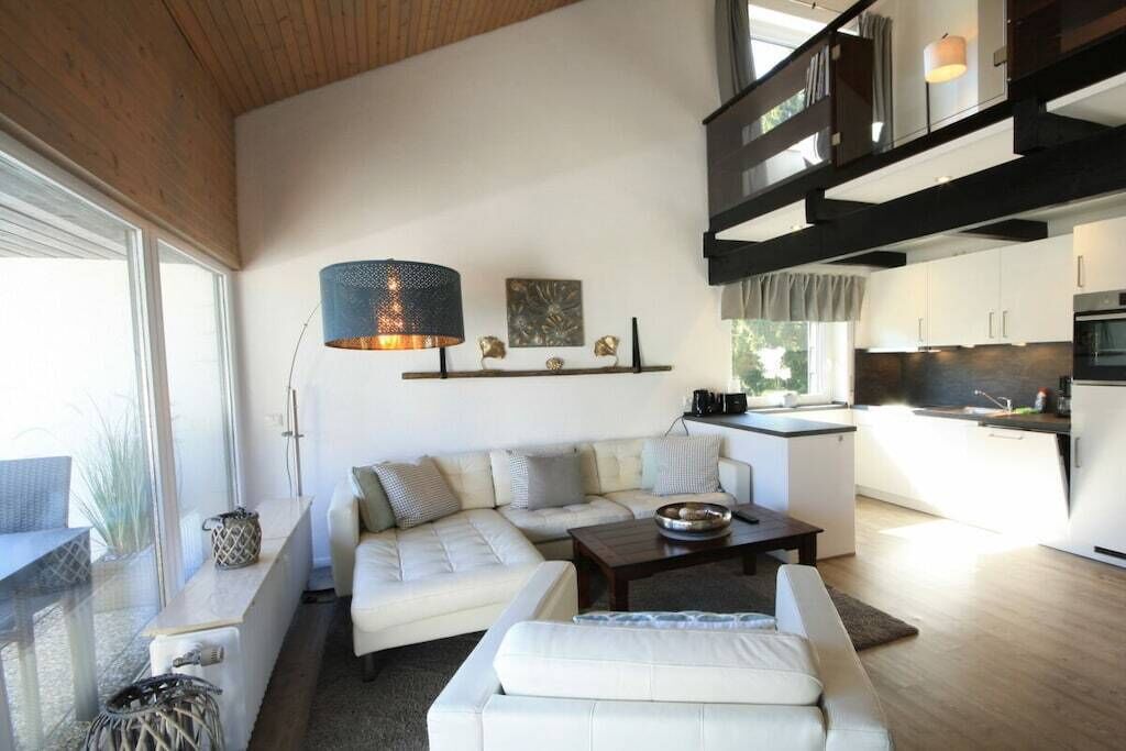 A modern living room with a sofa, coffee table, and a dining area with a kitchen in the background.