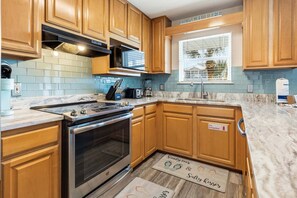 A kitchen with wooden cabinets, a stainless steel range, and a window with a view of palm trees. - KULULA- Sleeps 19, 6 BR 5 BA, private pool, bikes & beach (Santa Rosa Beach)