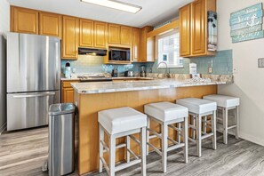 Una cocina con armarios de madera, un refrigerador de acero inoxidable, un microondas y una barra con taburetes.