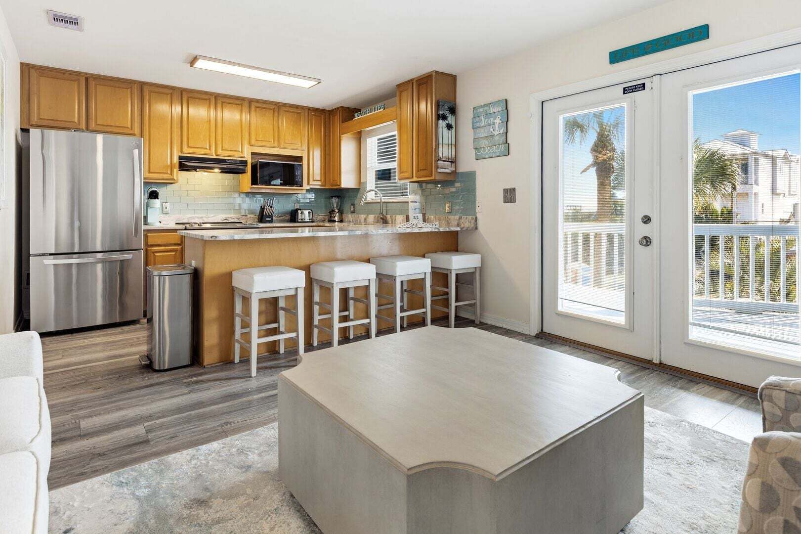 A modern kitchen with wooden cabinets, a stainless steel refrigerator, a microwave, and a bar area with stools.