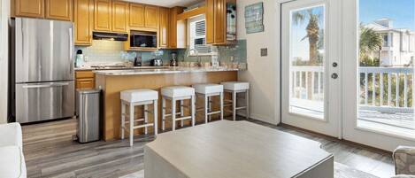 A modern kitchen with wooden cabinets, a stainless steel refrigerator, a microwave, and a bar area with stools.