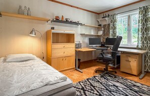 Ein gemütlicher Raum mit einem Bett, einem Schreibtisch mit zwei Bildschirmen, einem Stuhl und einer kleinen Ablagefläche mit Dekorationen.