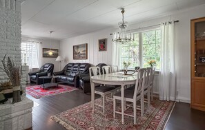 Un salon comprenant un coin repas, agrémenté d’un lustre, de fauteuils en cuir, d’une table blanche et d’un tapis à motifs rouges.