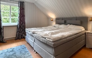 Une chambre à coucher avec un grand lit, une table de chevet, une lampe et une fenêtre avec des rideaux.