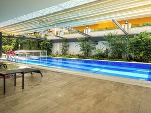 A swimming pool with a tiled edge, surrounded by greenery and a covered area with a railing. - Qoople Cleopatra Exclusive - Cozy 1-bedroom apartment in Alanya (Alanya)